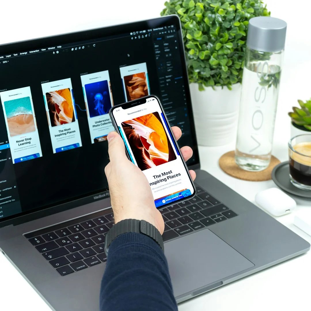 Une main tenant un smartphone au-dessus de croquis de conception d’application sur des feuilles, vue de dessus.